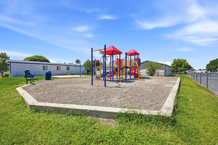 Modern recreational area featuring a multi-level composite playground structure with red accents and blue support posts, set within a concrete-bordered safety surface