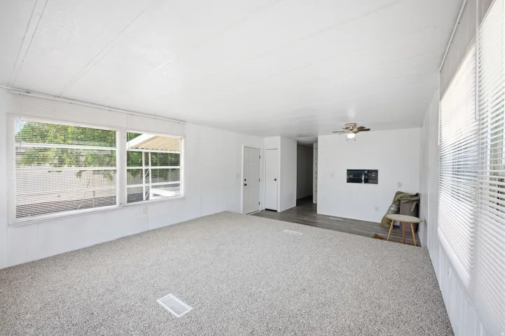 Spacious interior featuring light-toned carpet flooring, multiple windows with horizontal blinds, a white paneled ceiling, and a ceiling fan