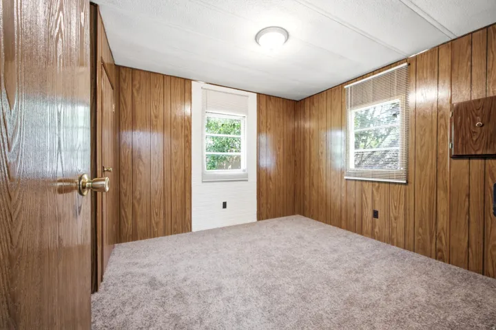 Room featuring wood paneling on walls, two windows with blinds, and a built-in wall cabinet