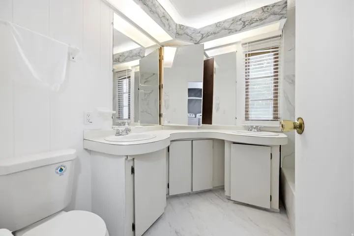 Bathroom featuring a dual vanity with integrated sinks, white cabinetry, and a full mirror wall