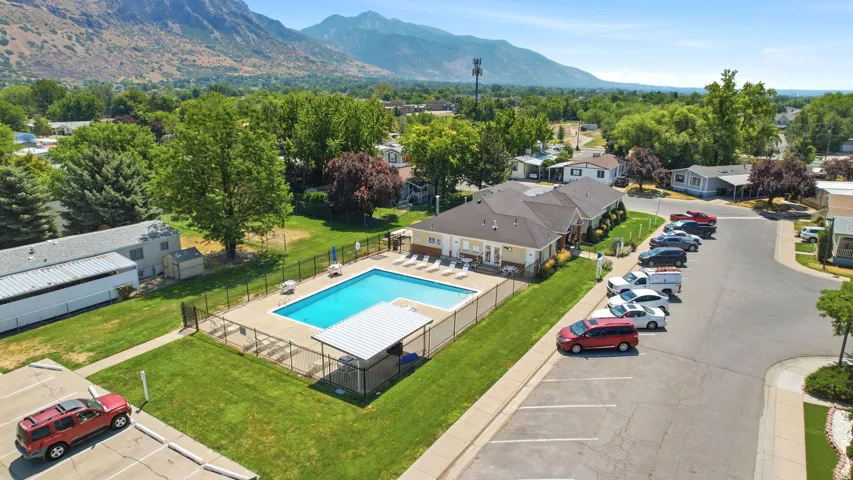 Resort-style community amenity featuring a sparkling saltwater pool with surrounding lounge deck, manicured lawn with mature shade trees, and gated parking area
