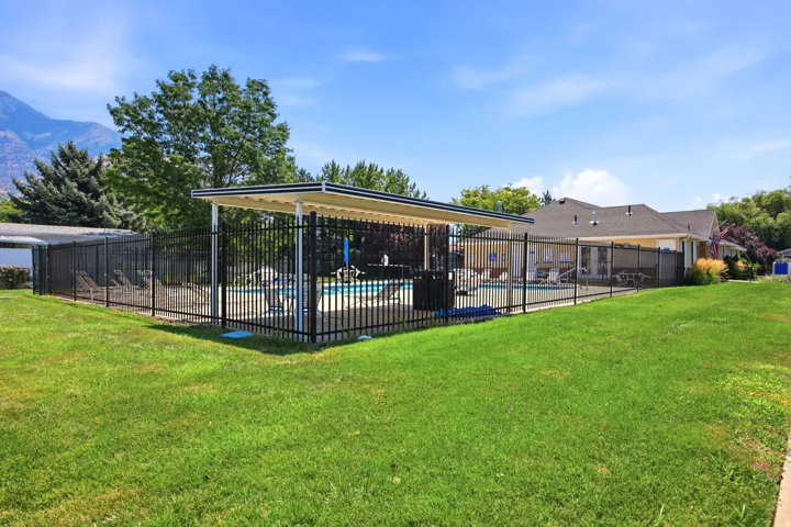Expansive backyard oasis featuring a fully enclosed black metal-framed pavilion with integrated shade structure, manicured lawn, mature landscaping with mixed tree coverage, and mountain backdrop