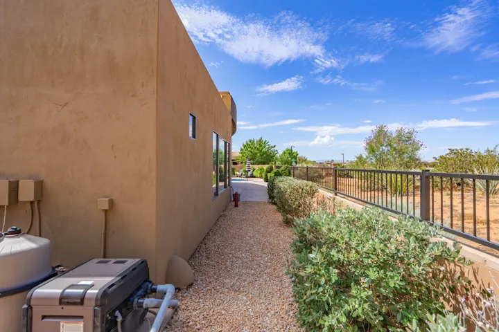 Stucco exterior with multiple windows, featuring a gravel pathway, mature landscaping, and a dark metal fence