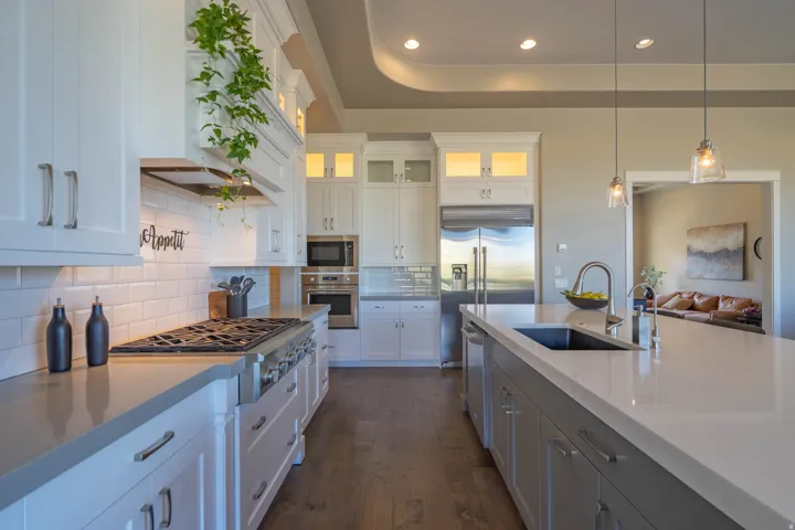 Gourmet kitchen featuring a large island with an undermount sink, stainless steel appliances, white subway tile backsplash, wood-finish flooring, and recessed lighting