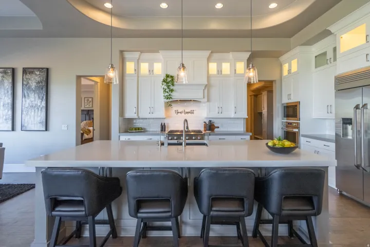 Kitchen featuring a large central island with seating for four, white shaker-style cabinetry with upper glass-front illuminated cabinets, stainless steel appliances, and a tile backsplash