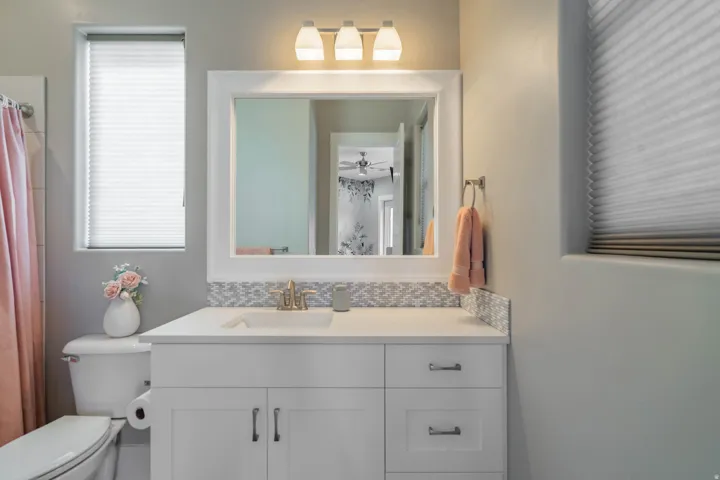 White shaker-style vanity with a single basin, a light-toned countertop, and a decorative tile backsplash