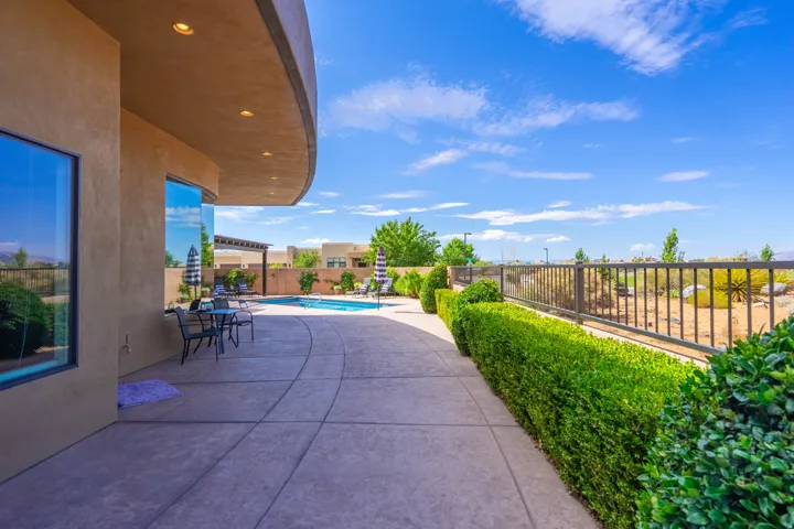 Curved stucco exterior with large windows, an expansive concrete patio, and a built-in swimming pool