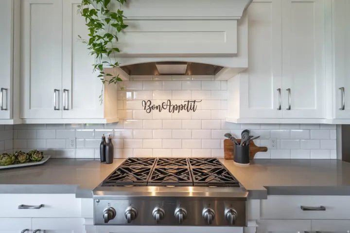 Stainless steel gas range beneath a custom range hood, framed by white shaker-style cabinetry