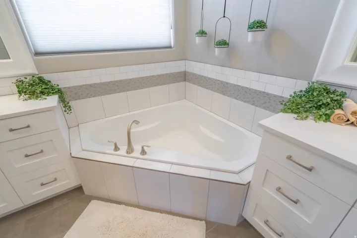 Corner soaking tub with brushed nickel fixtures, surrounded by white subway tile and a mosaic accent band