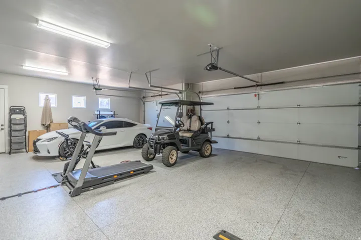 Spacious multi-car garage featuring an epoxy-coated concrete floor, two overhead doors, and multiple ceiling-mounted fluorescent light fixtures