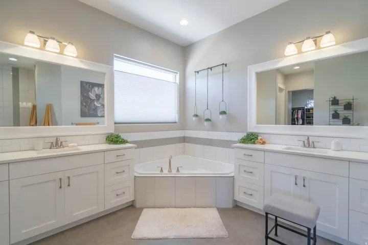 Expansive bathroom featuring a corner soaking tub, dual vanity areas with white cabinetry and undermount sinks, a large mirror over each vanity, and a window with a cellular shade