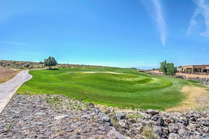 Golf course green with undulating terrain, paved cart path, and distant desert landscaping