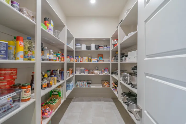 Spacious walk-in pantry featuring extensive white shelving, tiled flooring, and a panel door with a brushed nickel lever handle