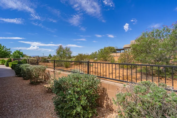 Outdoor space featuring a gravel pathway, established perimeter landscaping, and a black metal fence atop a block wall