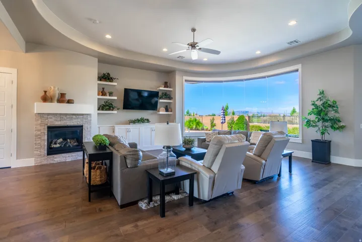 Spacious living area featuring a curved bank of windows, wood-finish flooring, and a stacked stone fireplace with a white mantel