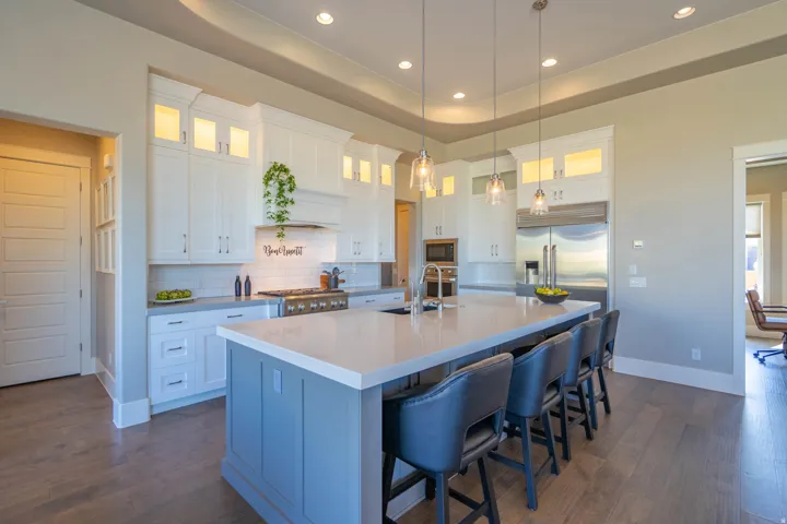 Spacious kitchen featuring an expansive central island with seating, white upper and lower cabinetry, stainless steel appliances, and wood-finish flooring