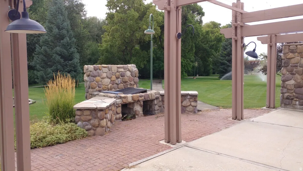 Outdoor entertaining area featuring a built-in stone barbecue, a pergola structure, and a brick paver patio