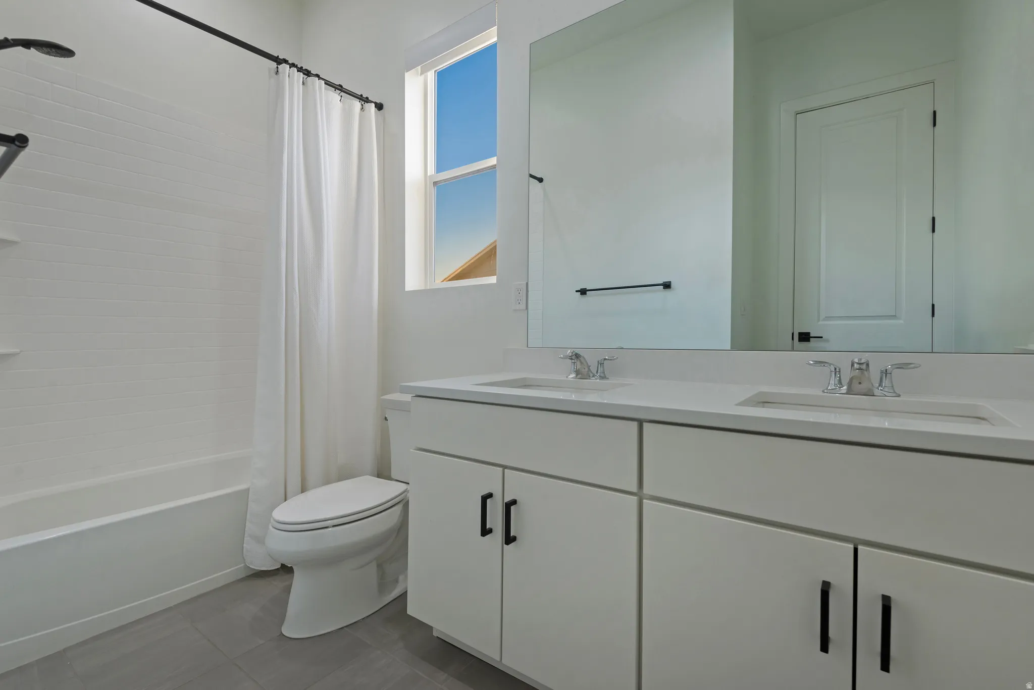 Double vanity featuring integrated sinks, white cabinetry with matte black hardware, and an expansive wall-mounted mirror