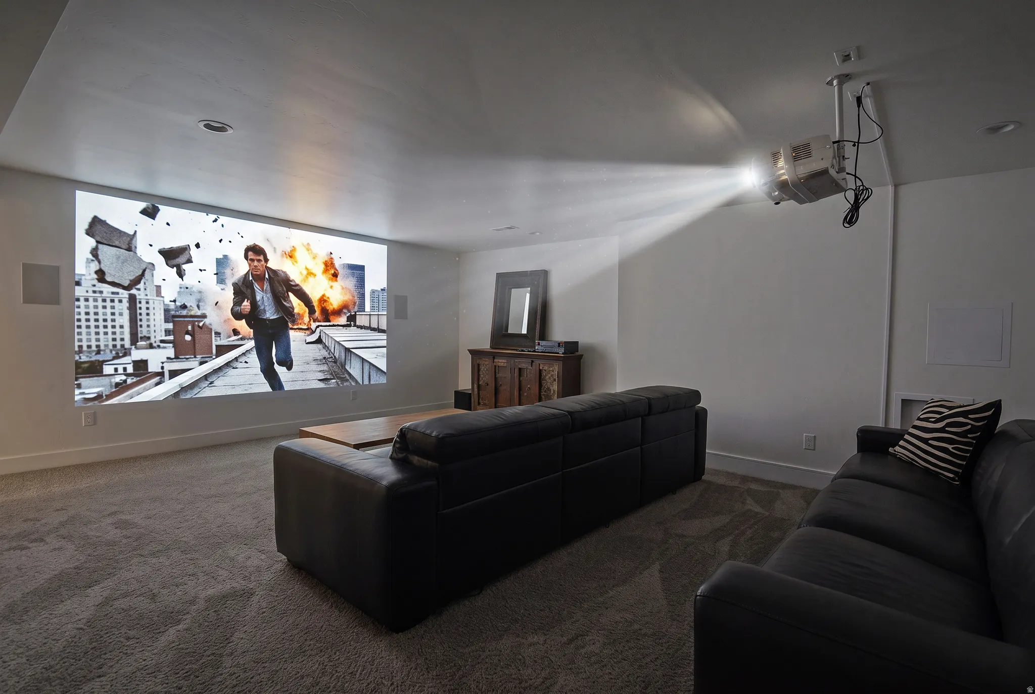 Dedicated media room featuring a large projection screen, mounted ceiling projector, built-in speakers, recessed lighting, and plush carpeting