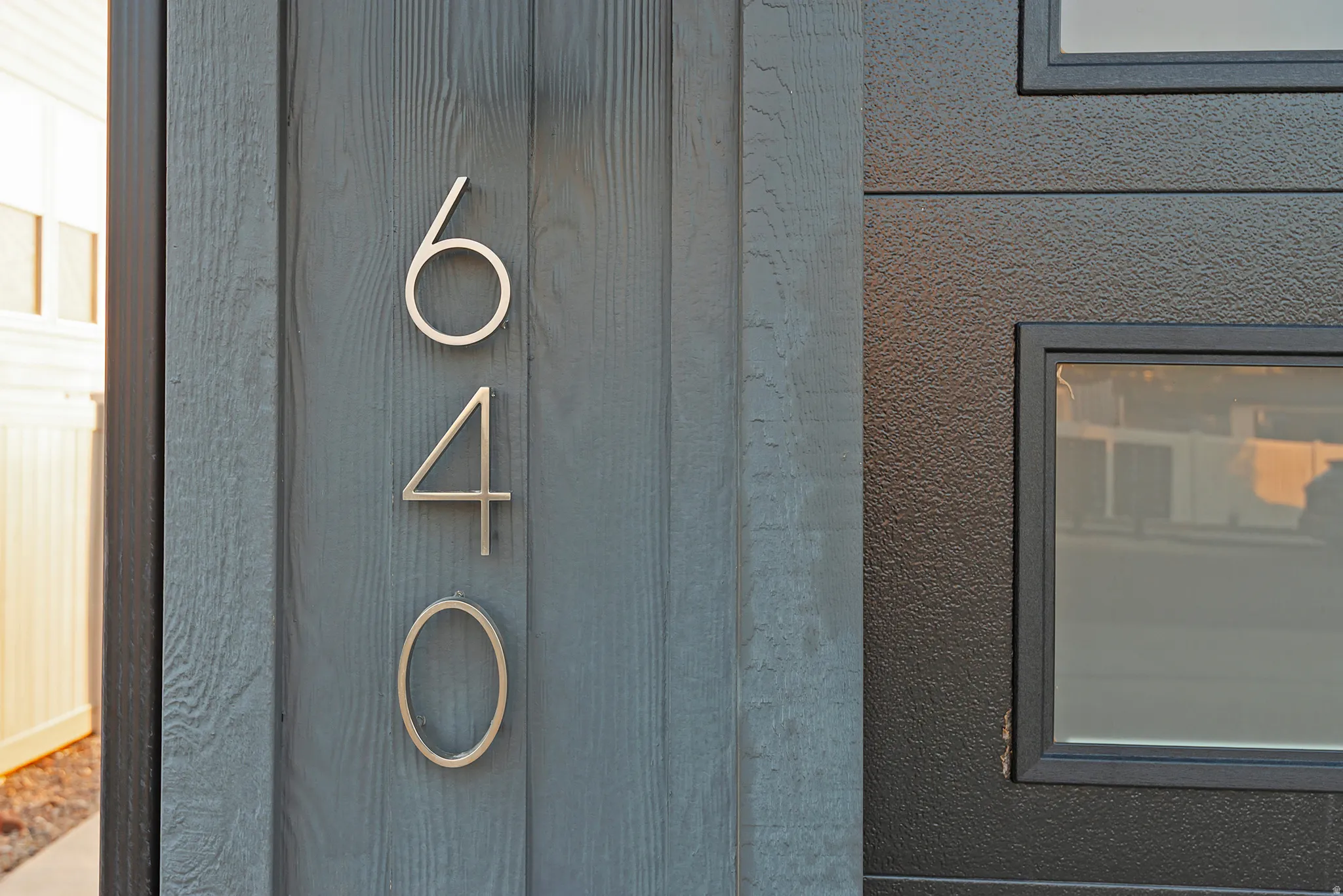 House numbers in a contemporary metallic finish against wood-finish siding, complemented by a textured exterior panel with integrated windows