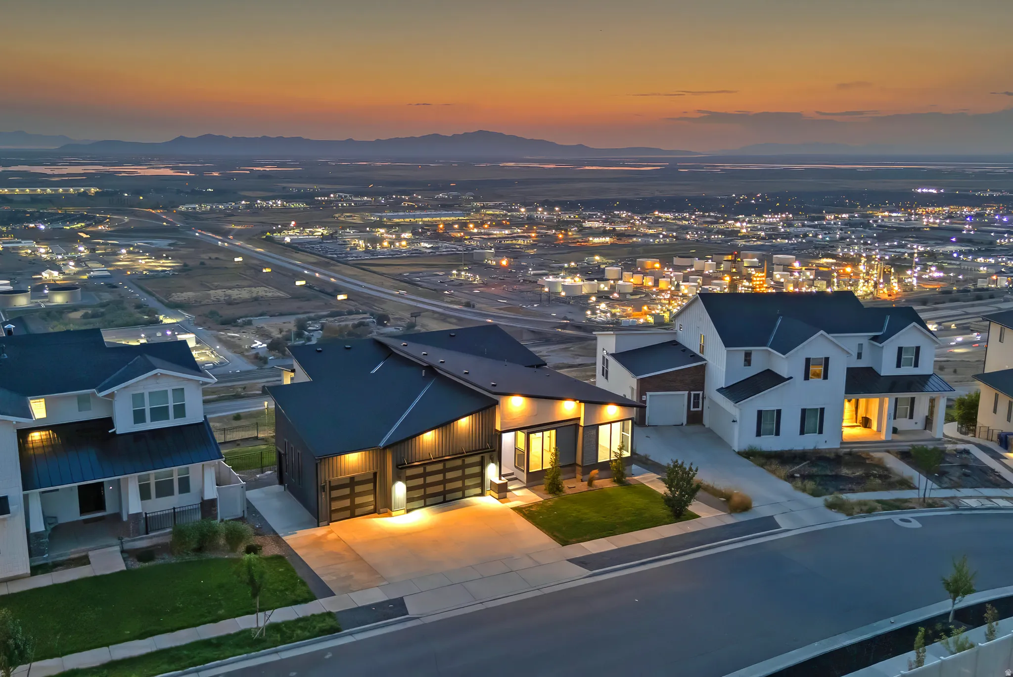 Modern home featuring a dark exterior, multiple garages, and illuminated entryways