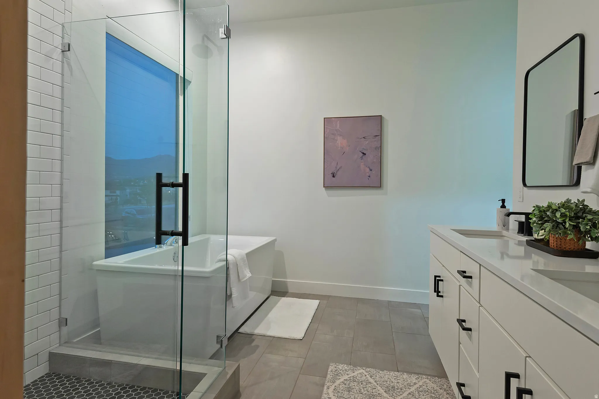 Contemporary bathroom featuring a freestanding tub, glass-enclosed shower with subway tile, double vanity with solid surface countertops, and dark-finish hardware