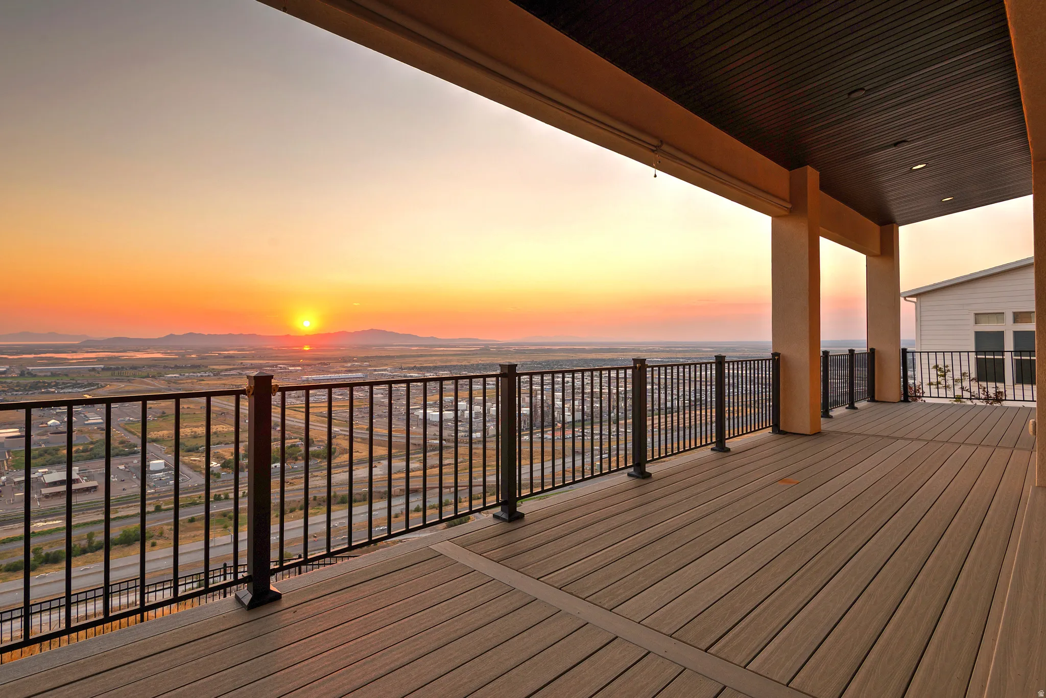 Expansive covered balcony featuring composite decking, a black metal railing, and substantial support columns