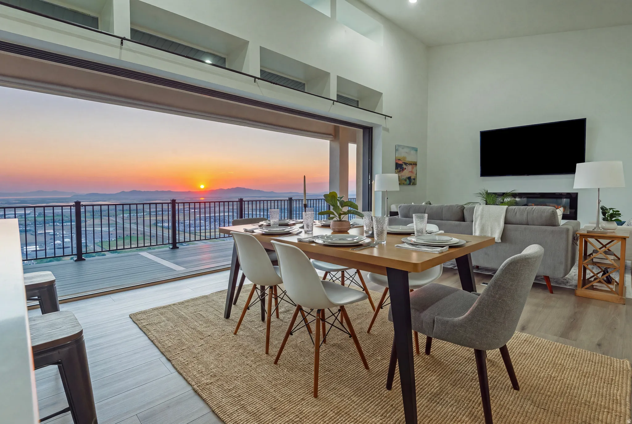 Expansive open-concept living area featuring a large dining space, high ceilings, and a retractable glass door system opening to a balcony with mountain and city scenery