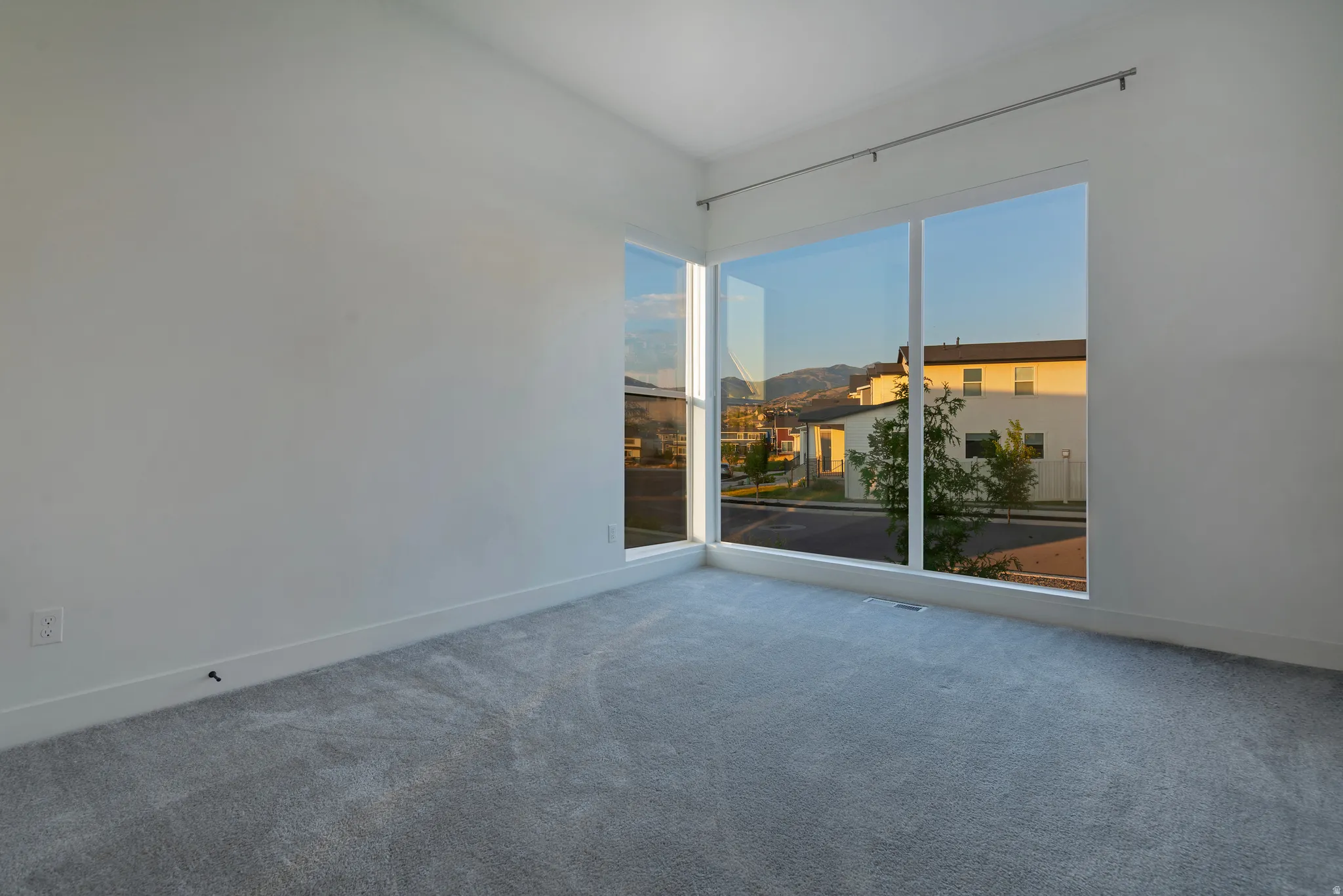 Corner room featuring expansive windows, neutral wall tones, plush gray carpeting, and white baseboards