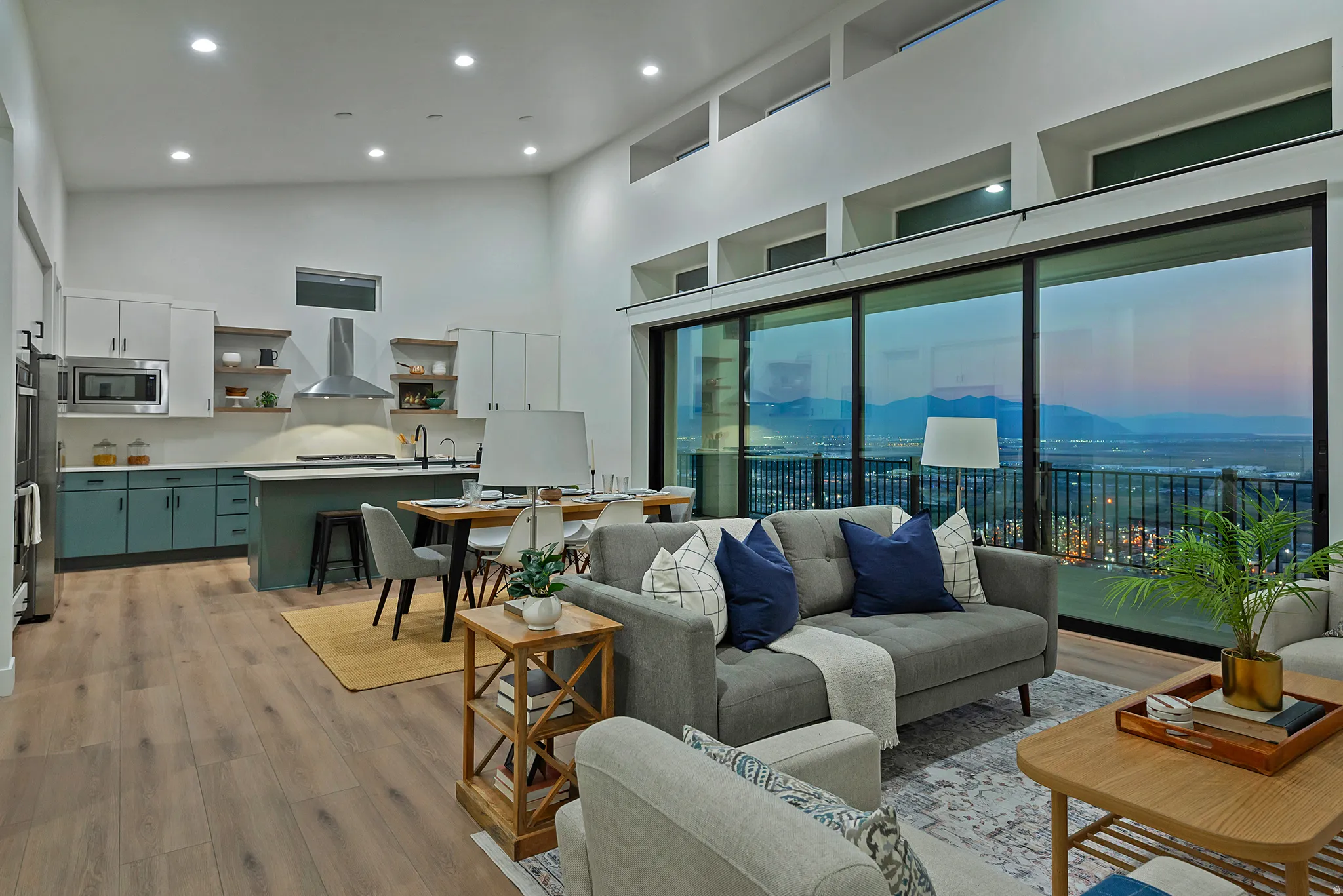 Open-concept living area with expansive sliding glass doors, high ceilings, wood-finish flooring, a contemporary kitchen featuring two-tone cabinetry, and an island with bar seating