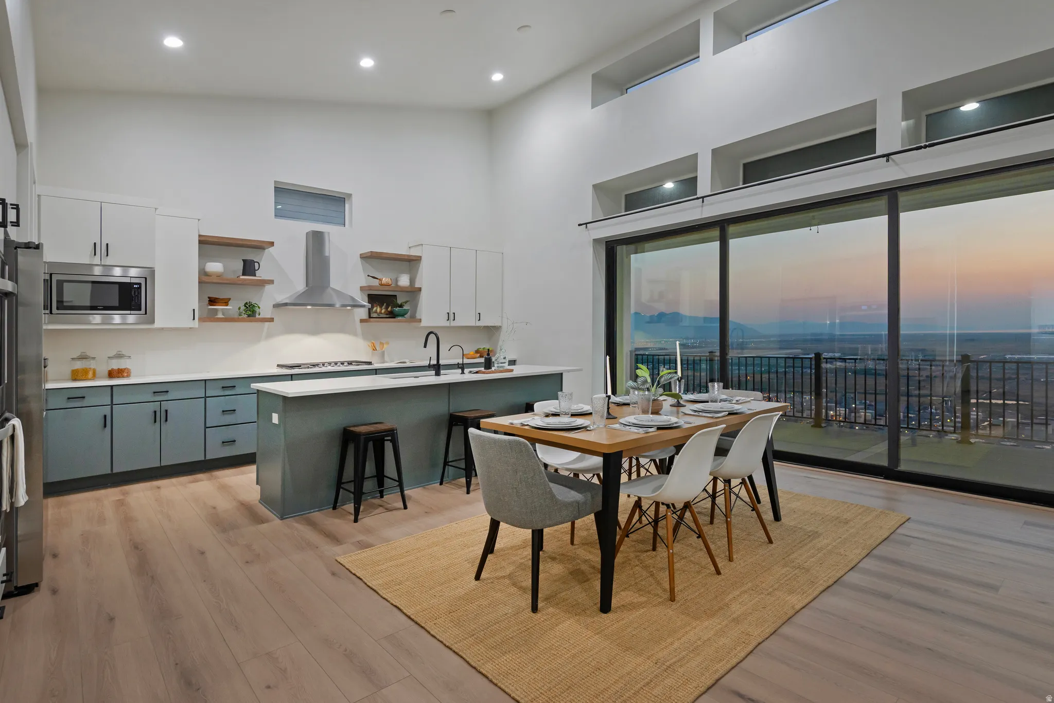 Open-concept kitchen and dining area featuring high ceilings, wood-finish flooring, a contemporary kitchen island, and a wall of glass doors leading to an exterior balcony