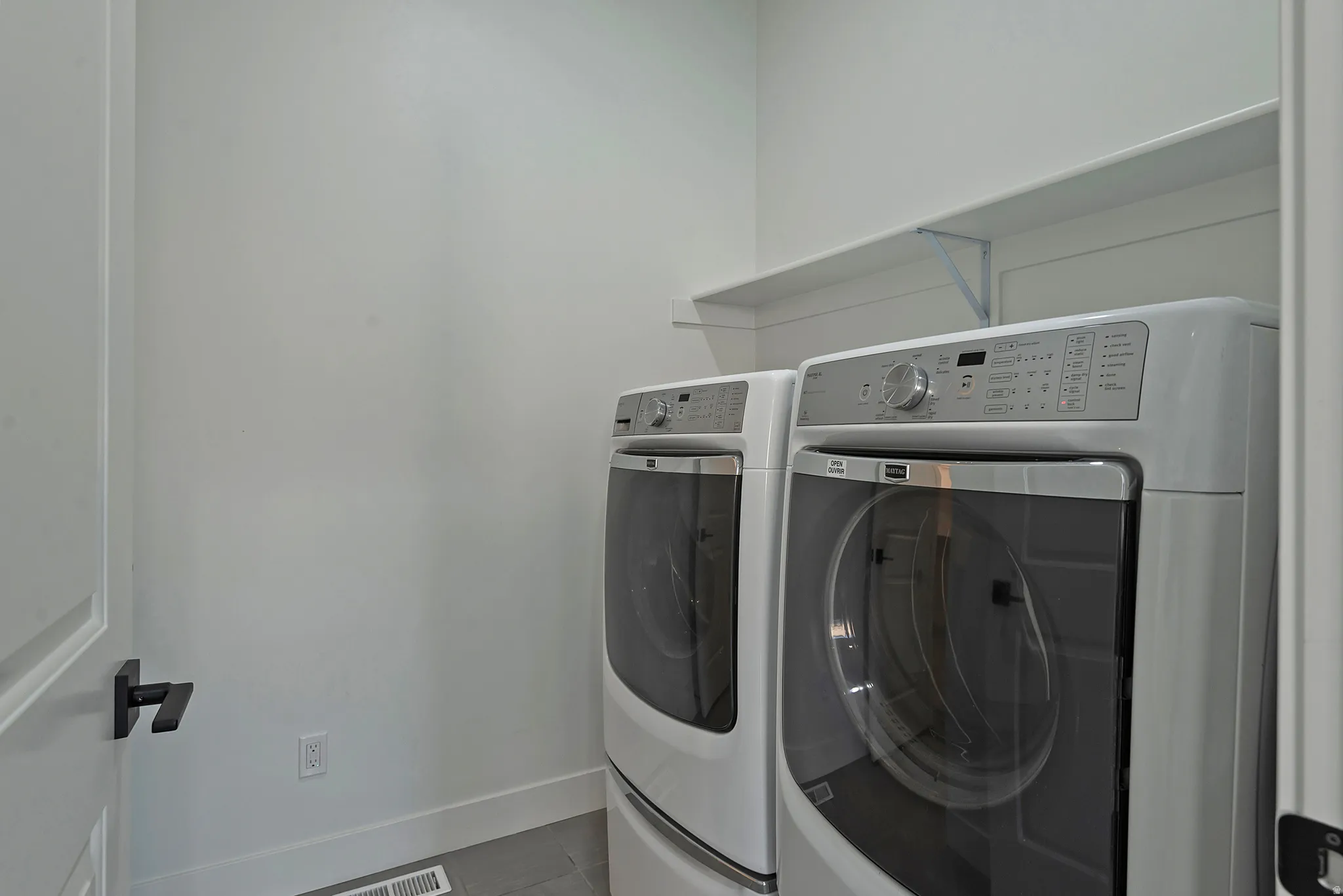 Dedicated laundry area featuring a white floating shelf, light gray flooring, and crisp white walls