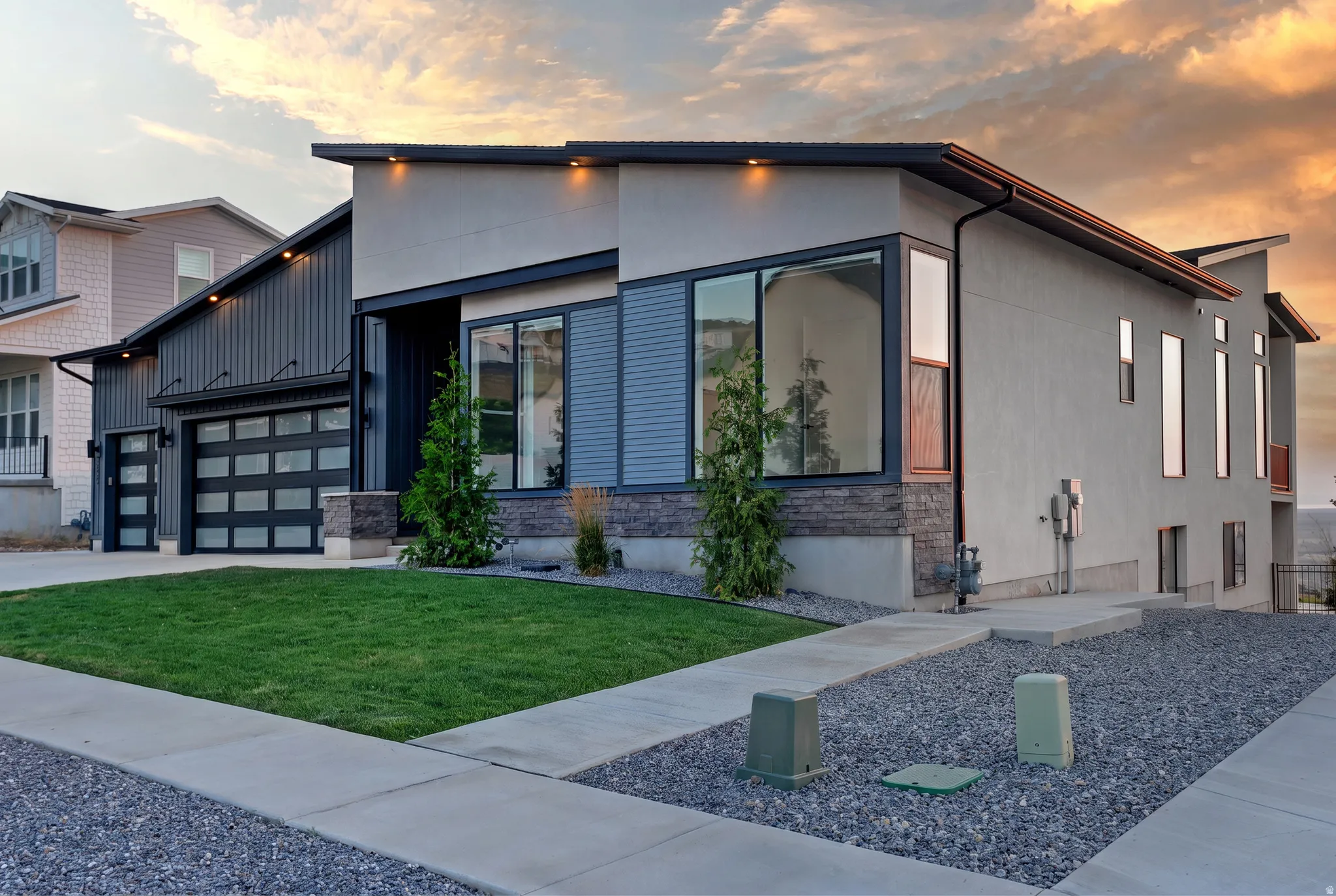 Contemporary facade featuring a prominent two-car garage with frosted glass panels, an additional single-car garage, and a combination of stucco and vertical siding