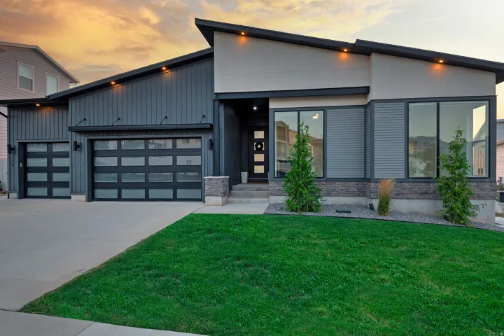 Modern exterior featuring vertical siding, large format windows, a stone facade accent, and two contemporary garage doors with frosted glass panels