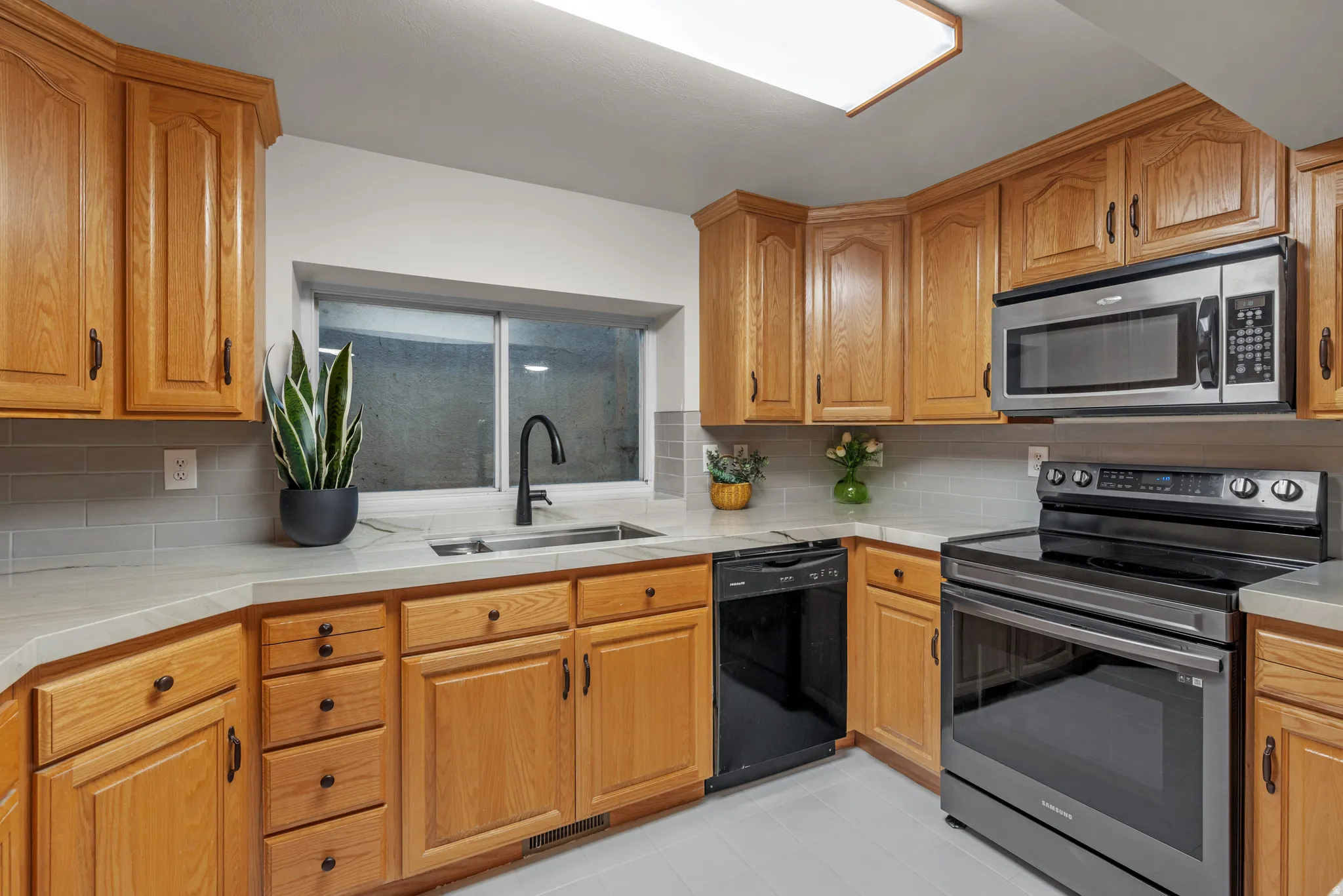 Kitchen featuring light wood cabinetry, light countertops, gray subway tile backsplash, and stainless steel appliances