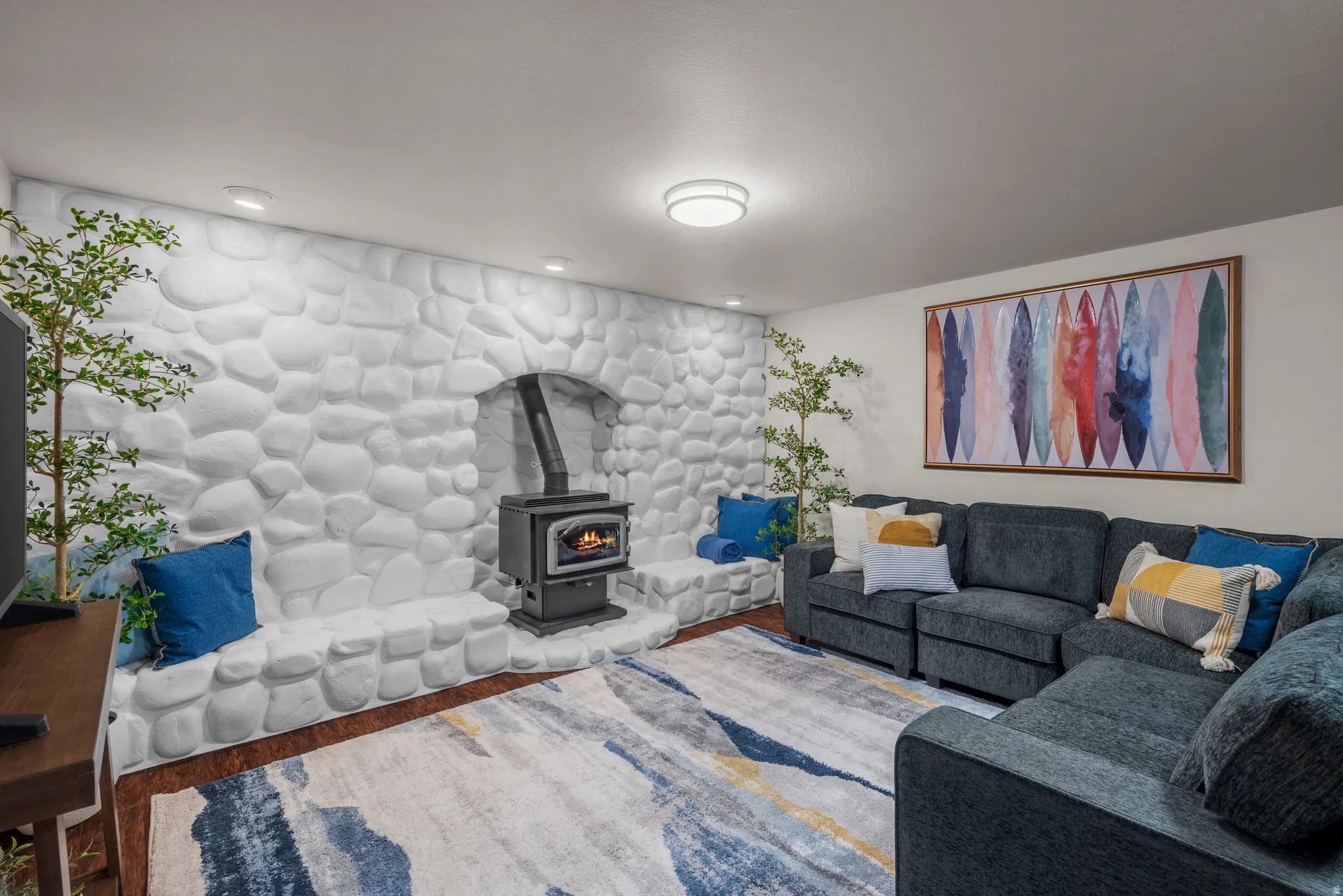 Living area featuring a stone accent wall with an integrated wood-burning stove, recessed lighting, and wood-finish flooring