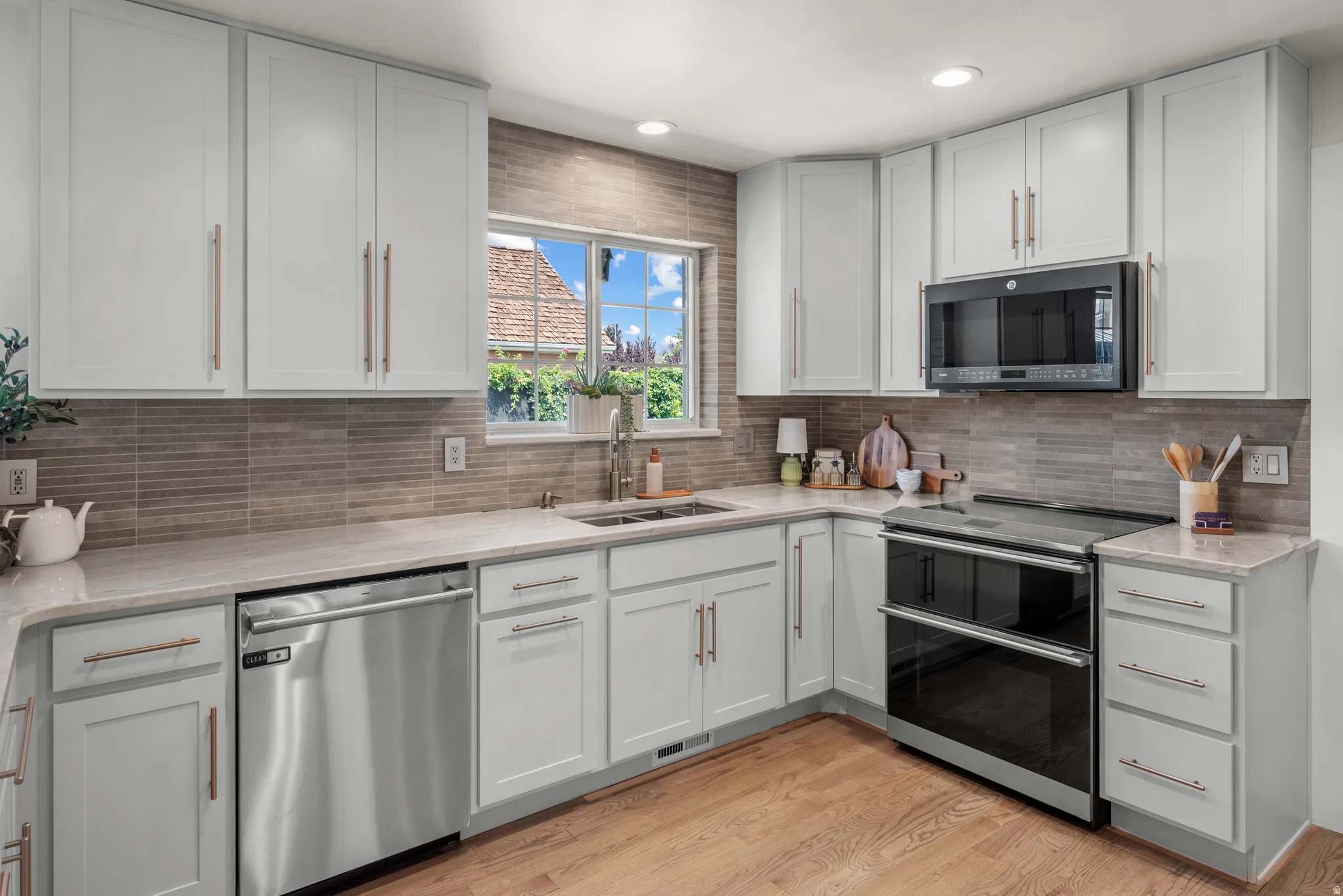 Kitchen featuring white shaker cabinetry, stainless steel appliances, light-toned countertops, and wood-finish flooring