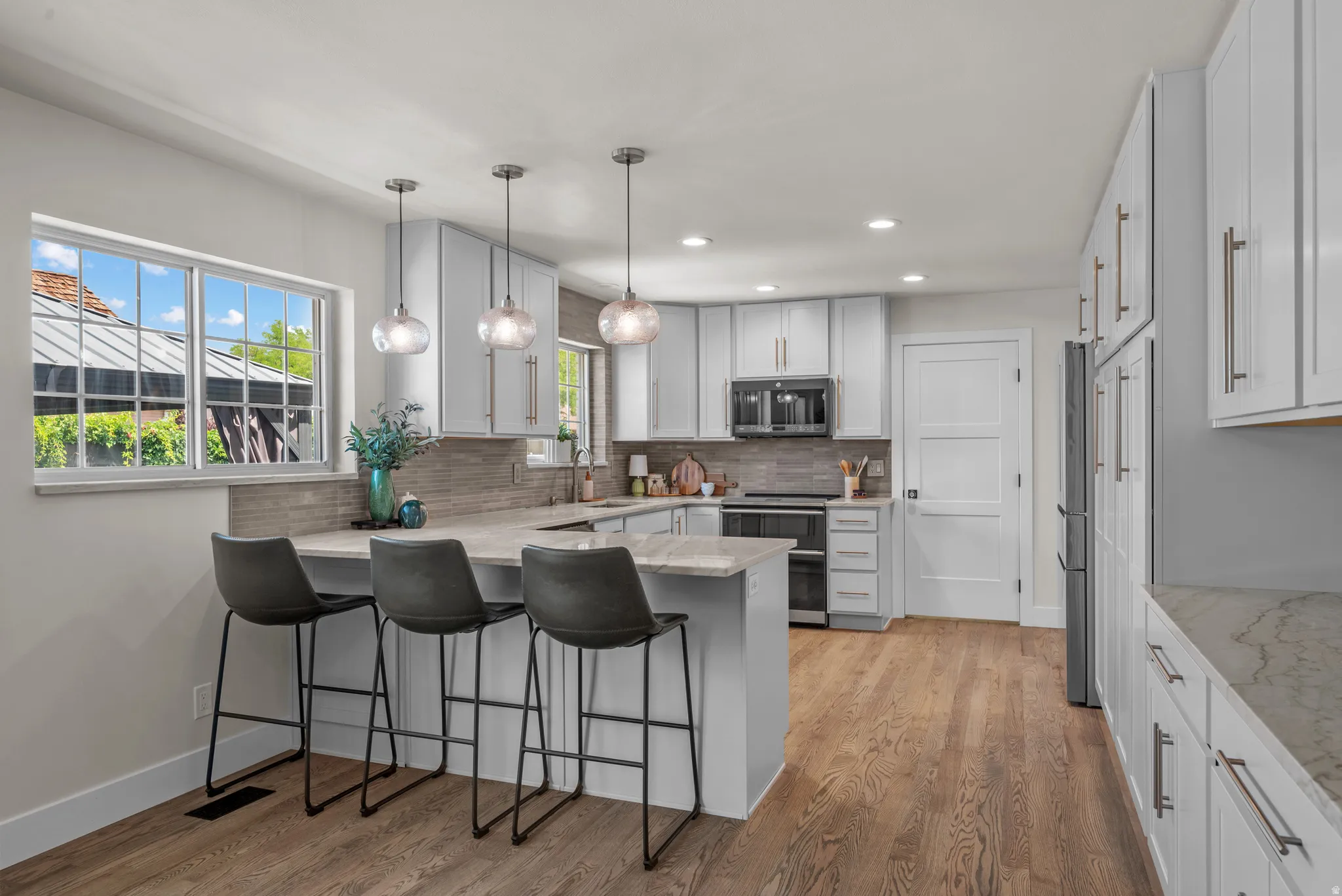 Contemporary kitchen featuring light wood-finish flooring, white cabinetry with brushed nickel hardware, and a center island with pendant lighting