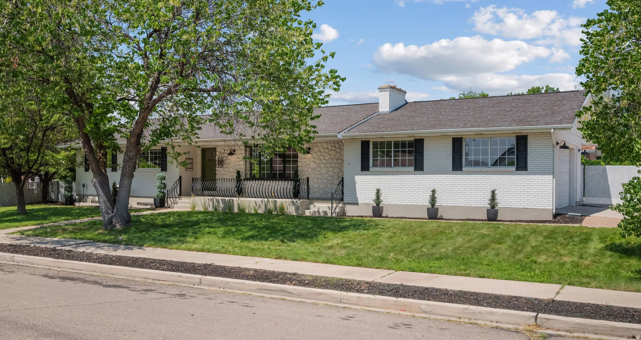 White brick and stone exterior featuring a dark asphalt shingle roof, black window shutters, a covered porch with wrought iron railings, and a manicured front lawn