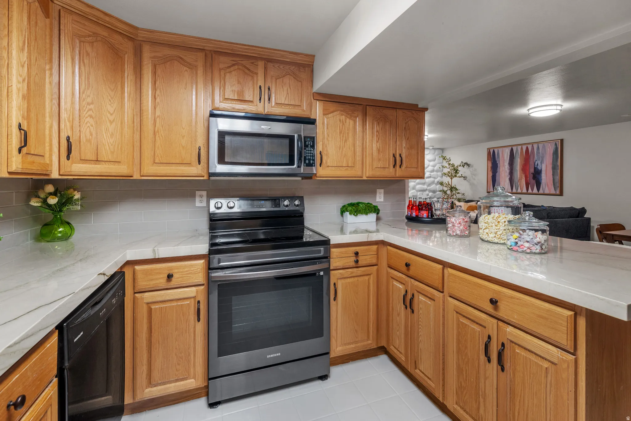 Kitchen featuring natural wood cabinetry, light-toned countertops, a subway tile backsplash, stainless steel microwave, and a black electric range