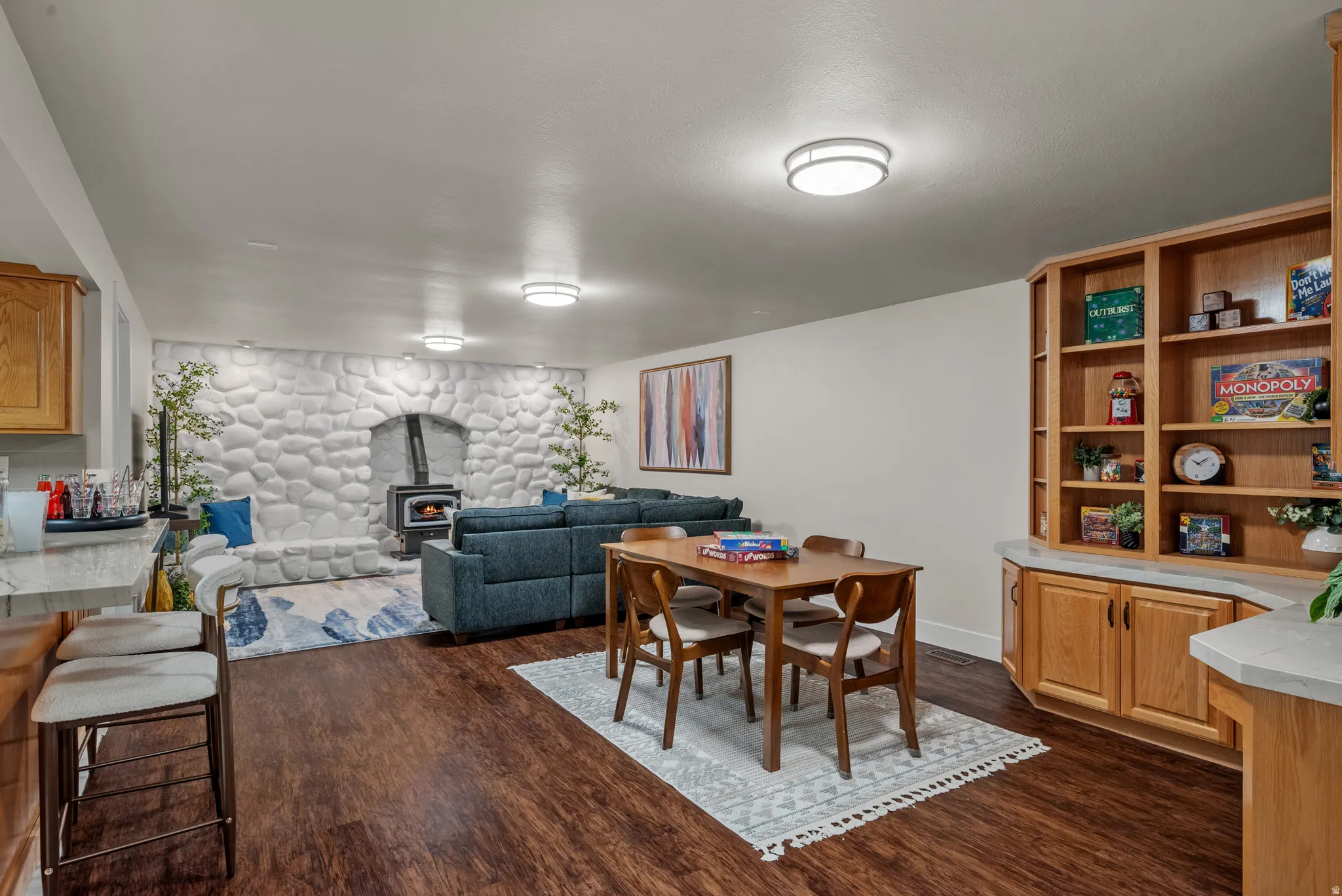 Spacious entertainment area featuring wood-finish flooring, a prominent stone-clad fireplace with a wood-burning stove, and built-in oak cabinetry