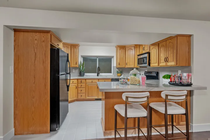 Kitchen featuring wood cabinetry, a black refrigerator, a black built-in microwave, and a black range