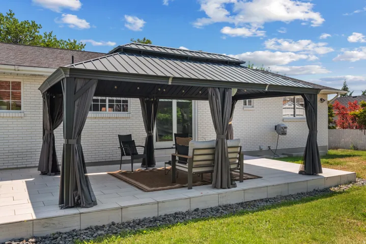 Spacious outdoor patio featuring a large gazebo with a metal roof and privacy curtains, set on a raised paver base