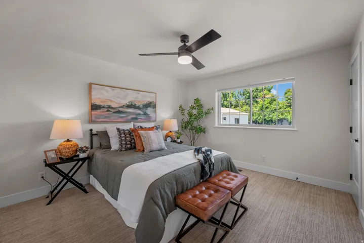 Bedroom featuring a ceiling fan with integrated lighting, a large window, light-toned carpeting, and white baseboards