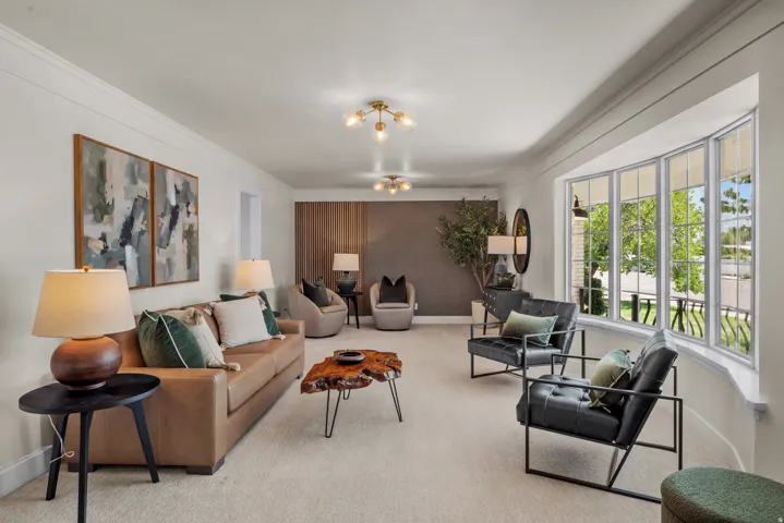 Spacious living area featuring a large bay window, crown molding, light-colored carpeting, and a wood-paneled accent wall