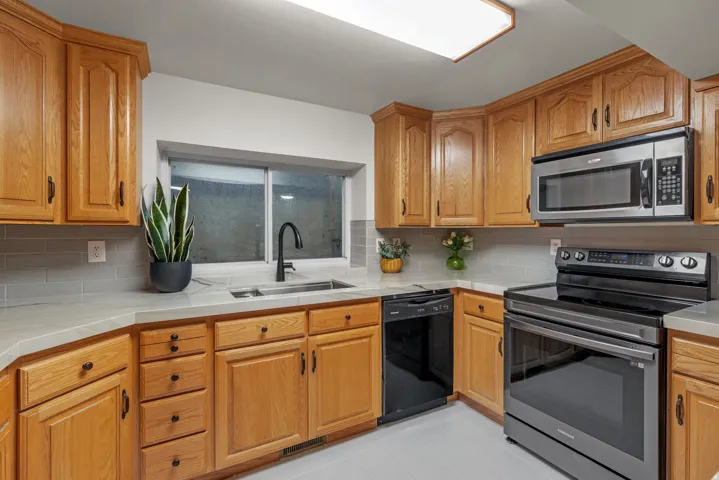 Kitchen featuring light wood cabinetry, light countertops, gray subway tile backsplash, and stainless steel appliances
