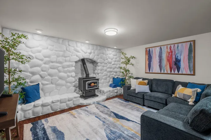 Living area featuring a stone accent wall with an integrated wood-burning stove, recessed lighting, and wood-finish flooring