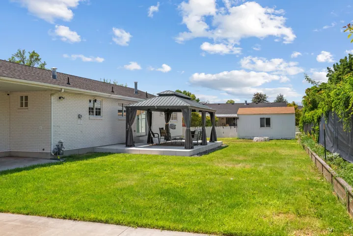 Spacious backyard featuring a covered patio with a dark grey gazebo, a large lawn, and a separate storage shed