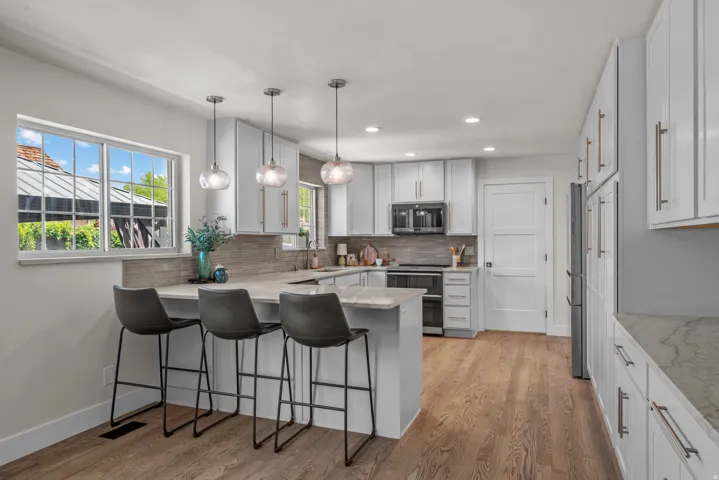 Contemporary kitchen featuring light wood-finish flooring, white cabinetry with brushed nickel hardware, and a center island with pendant lighting