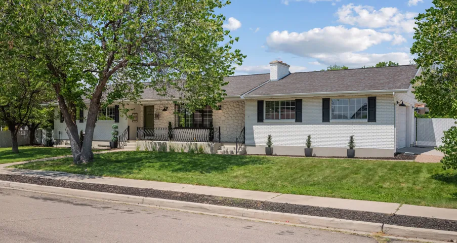 White brick and stone exterior featuring a dark asphalt shingle roof, black window shutters, a covered porch with wrought iron railings, and a manicured front lawn